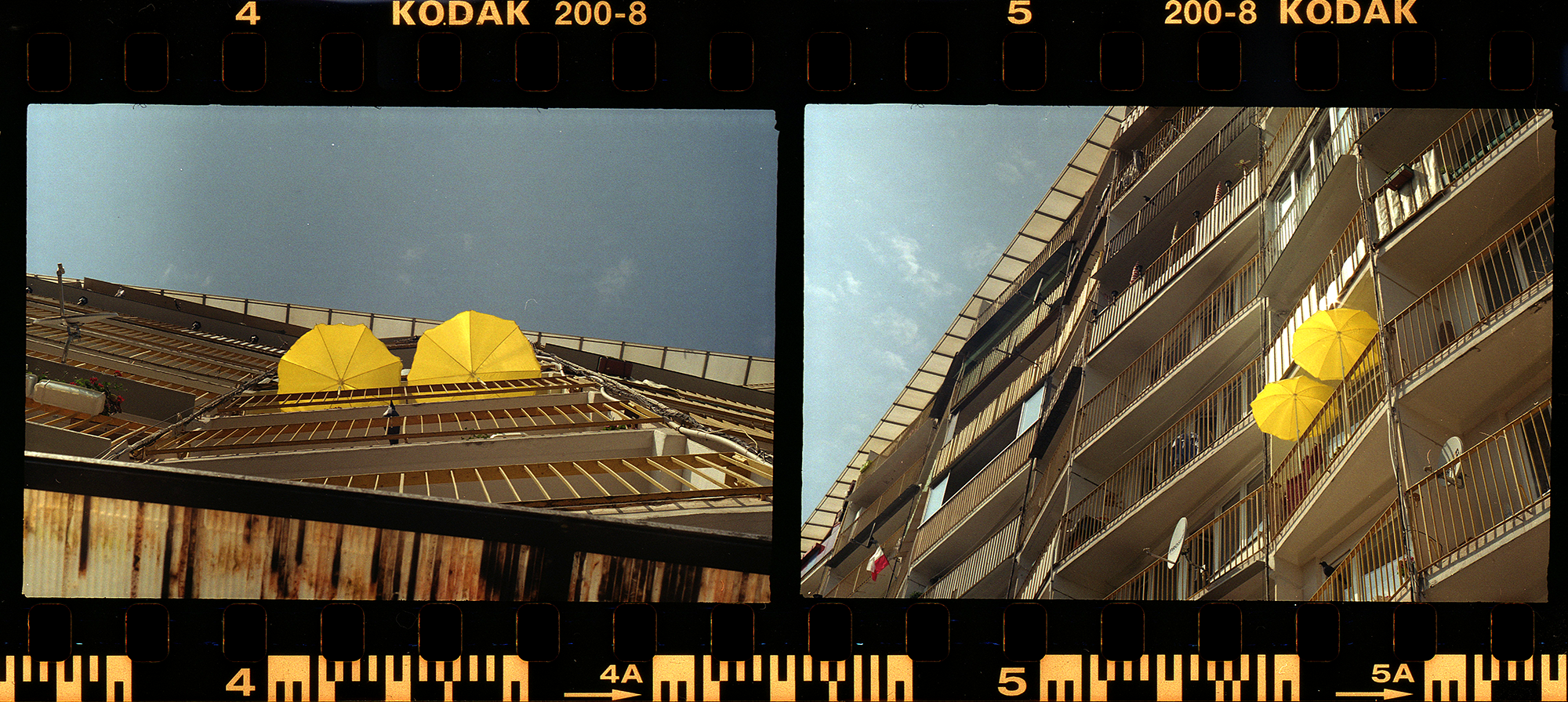 Analogowa fotografia architektury z żółtymi parasolami na balkonach